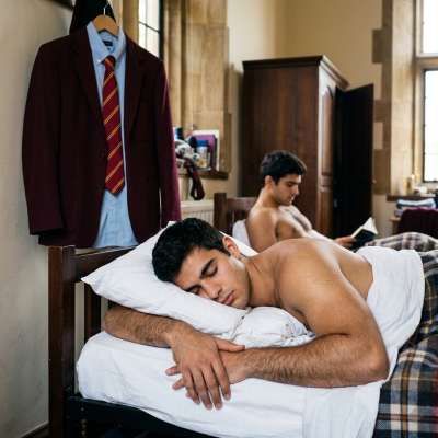 Unbuttoned blazer, crisp white sheets tangled around his thighs—perfection in dorm-room repose. The academy’s elite embrace...